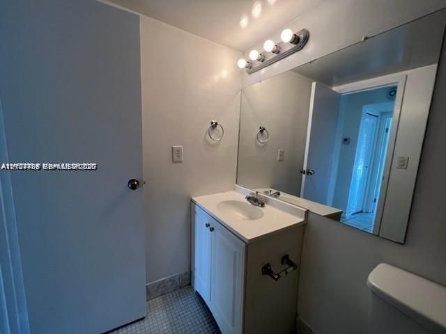 White vanity with an integrated sink and countertop, large wall-mounted mirror, four-light vanity fixture, and tiled flooring