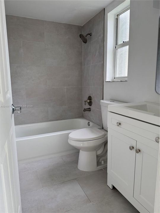 Bathroom featuring a white vanity cabinet with a integrated sink, gray tile surround for the tub, large-format floor tiling, and bronze-tone shower fixtures