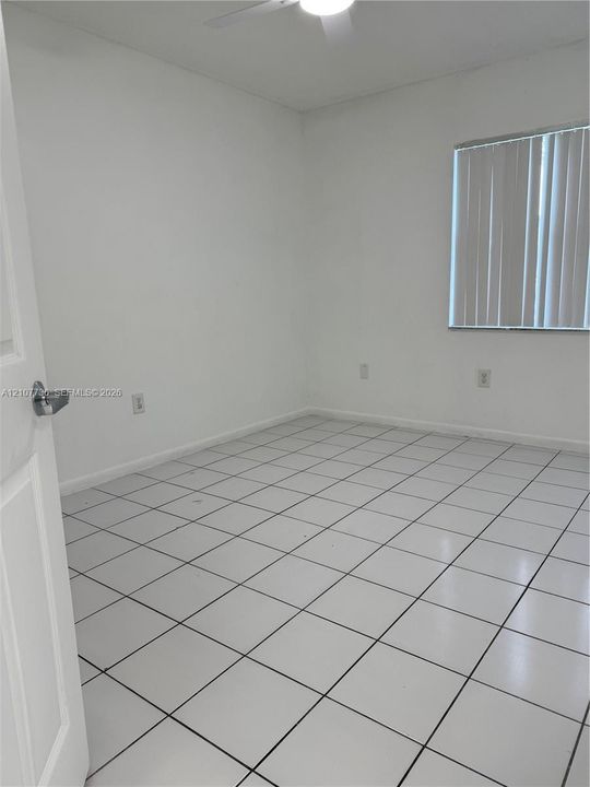 Neutral-toned room featuring ceramic tile flooring, vertical window blinds, and a ceiling fan with integrated lighting