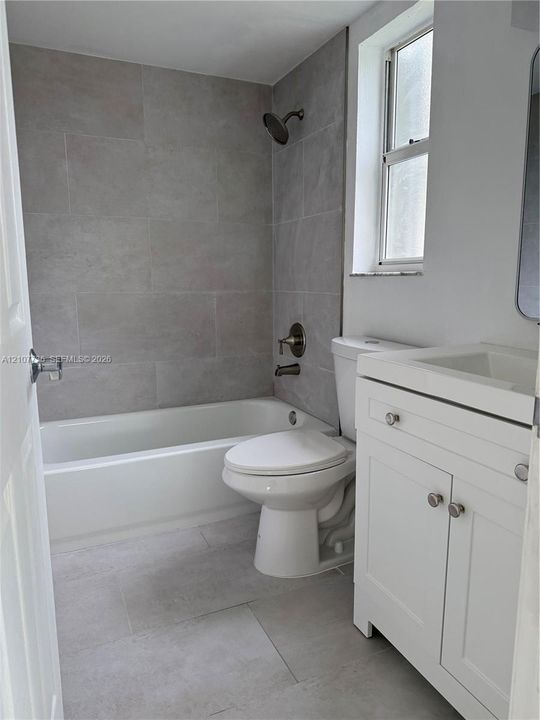 Bathroom featuring large-format gray tile shower surround, built-in soaking tub, white vanity cabinet, and oil-rubbed bronze fixtures