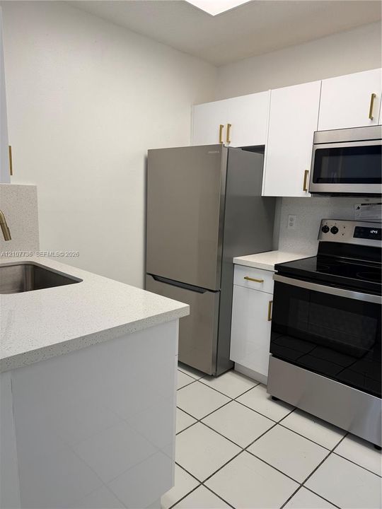 Kitchen featuring white cabinetry with metallic pulls, stone-composite countertops, stainless steel appliances, and tile flooring