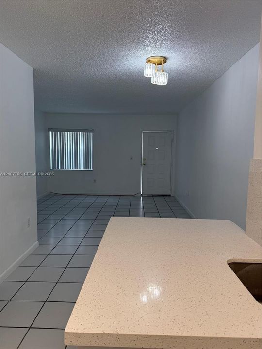Solid surface countertop with a light speckled finish, neutral ceramic tile flooring, and a multi-light flush-mount fixture with glass shades