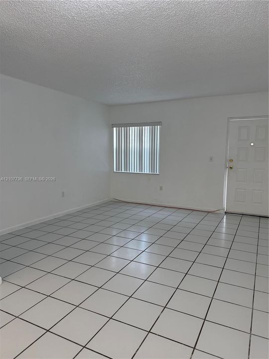 Neutral interior space featuring white walls, square ceramic tile flooring, and vertical window blinds