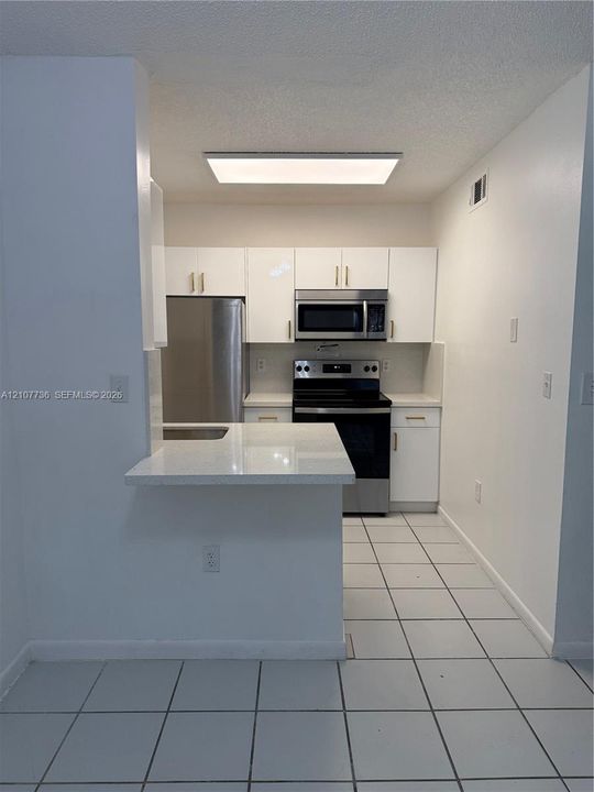 Kitchen featuring white cabinetry, solid-surface countertops, tile flooring, and a stainless steel appliance suite including a built-in microwave and range