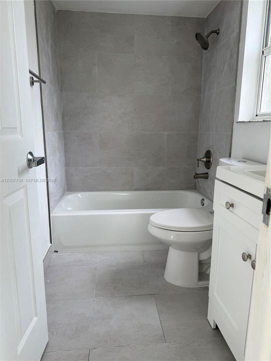 Bathroom featuring large-format gray tile flooring and wall surround, a white vanity with integrated basin, and brushed-finish fixtures
