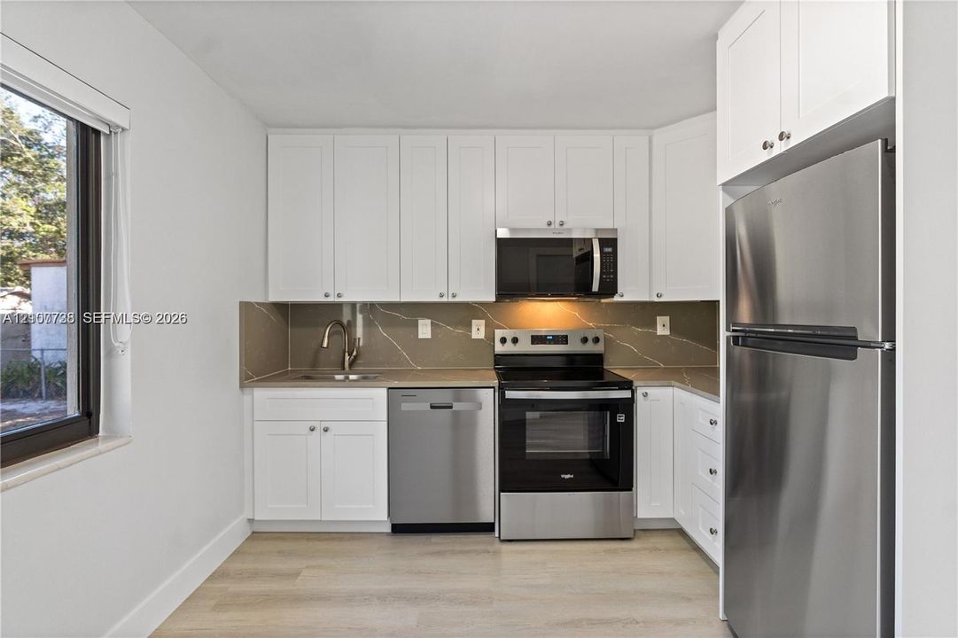 Kitchen featuring white Shaker-style cabinetry, stainless steel appliances, stone-finish countertops, full-height decorative backsplash, and light-toned wood-finish flooring