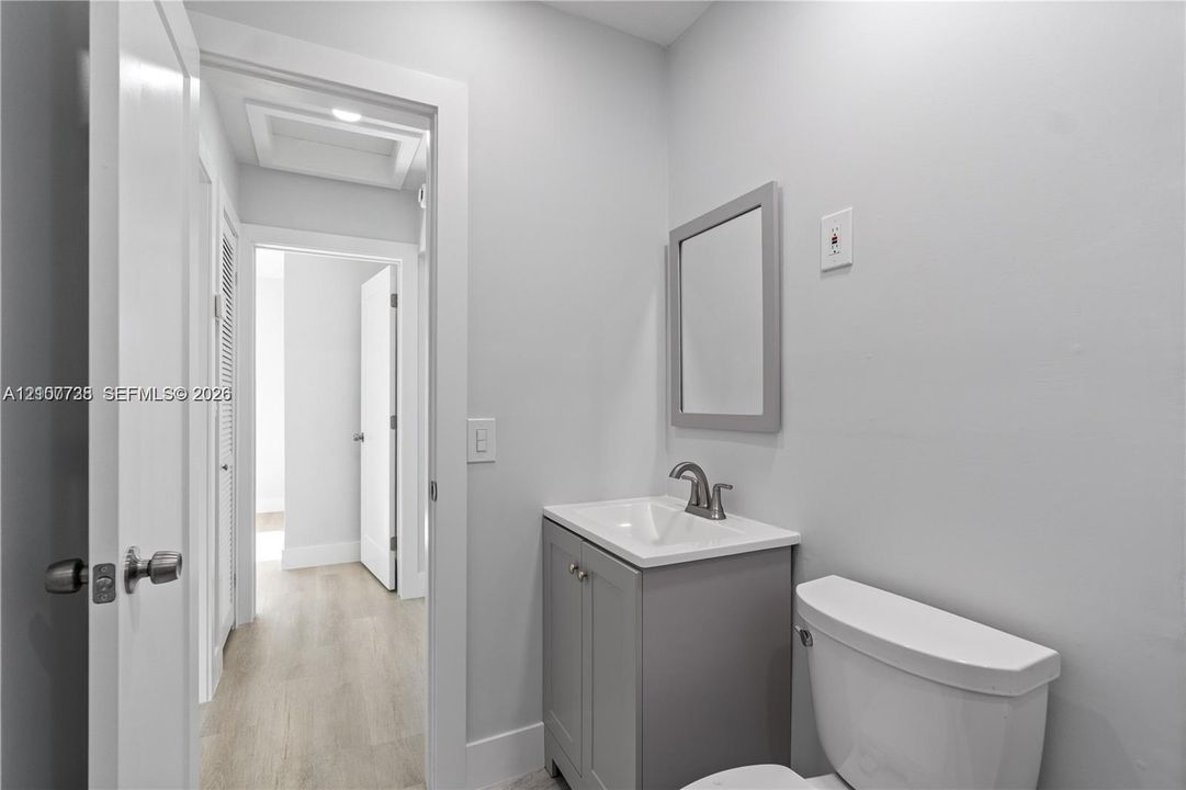 Grey vanity with a stone countertop, integrated sink, metal faucet, framed mirror, and wood-finish flooring