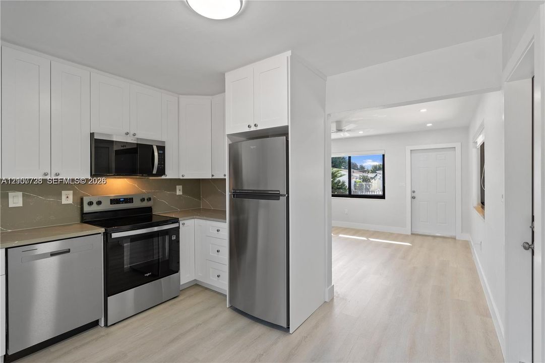 Kitchen featuring white shaker-style cabinetry, neutral stone-finish backsplash, stainless steel appliances, and light-toned wood-finish flooring