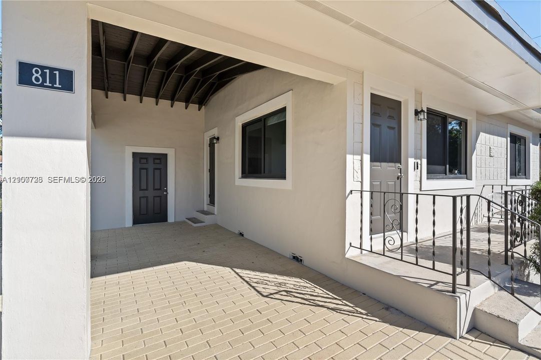 Covered entryway with paved flooring, concrete block exterior, decorative metal railings, and dual exterior doors