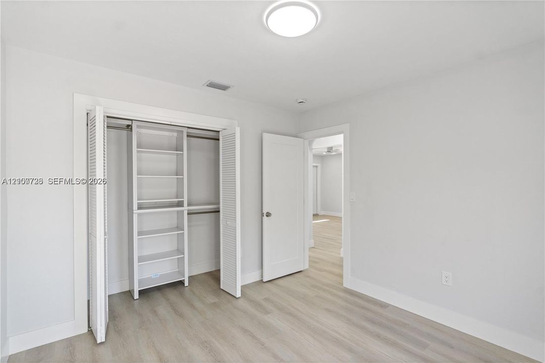 Interior space featuring wood-finish flooring, a closet with louvered doors and built-in shelving, and a flush-mount overhead light fixture