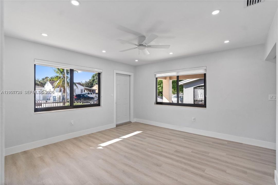 Interior room featuring neutral wall tones, wood-finish flooring, recessed lighting, a ceiling fan, and large windows with black frames