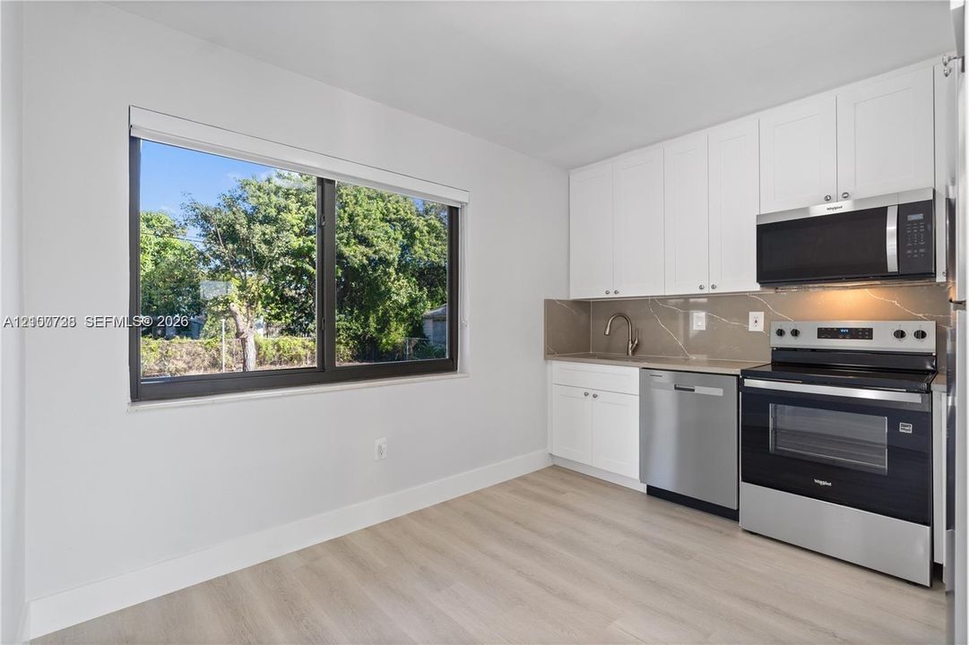 Kitchen featuring white shaker-style cabinetry, wood-finish flooring, stainless steel appliances, and solid surface backsplash