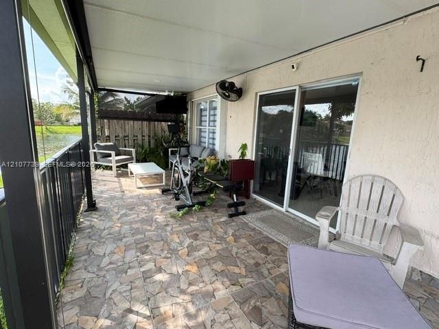 Covered patio featuring stone-tiled flooring, black metal railing, sliding glass doors, and a mounted wall fan