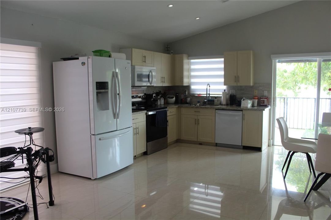 Kitchen featuring light-toned cabinetry, stone-finish countertops, stainless steel appliances, tile flooring, and vaulted ceilings