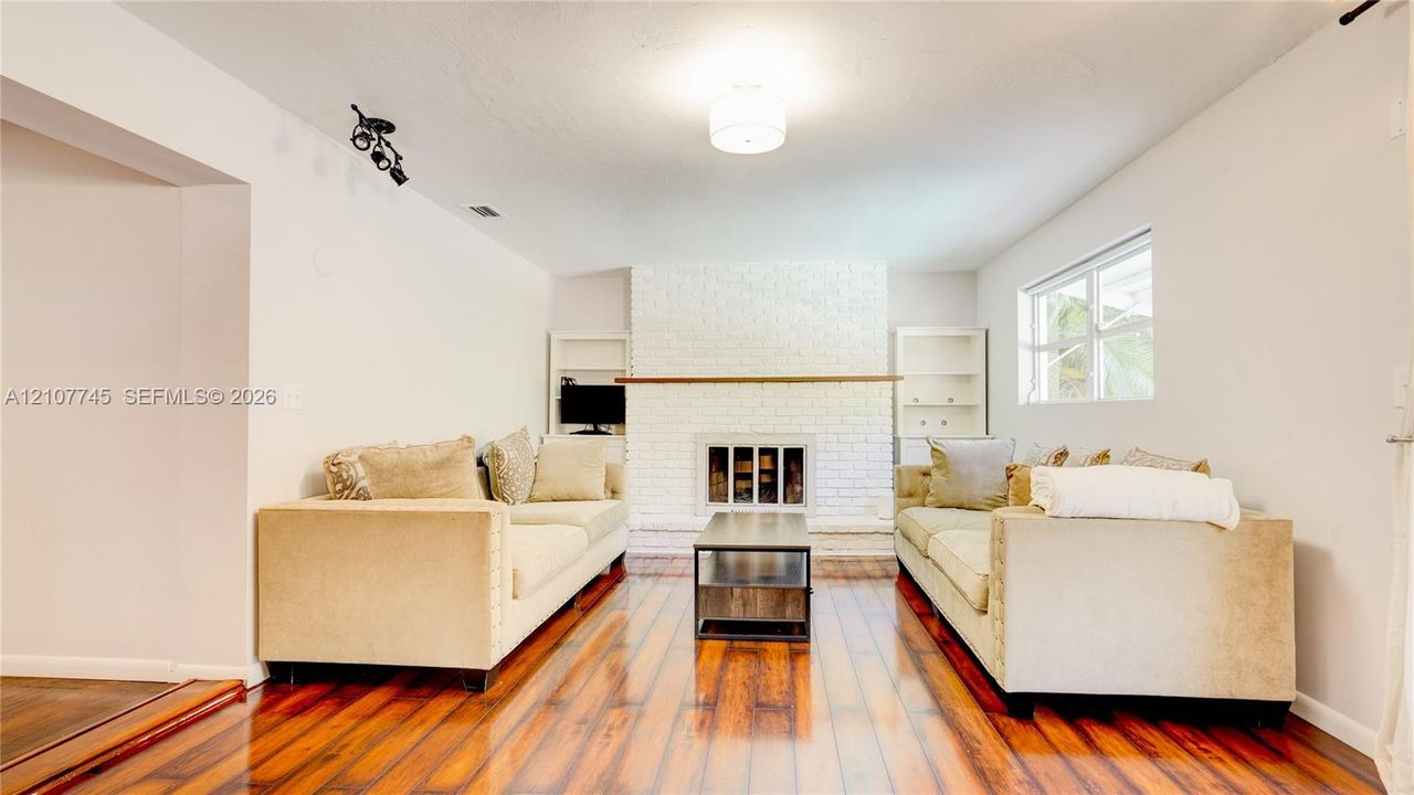 Interior space featuring wood-finish flooring, a white-painted brick fireplace with a wood mantel, and built-in shelving