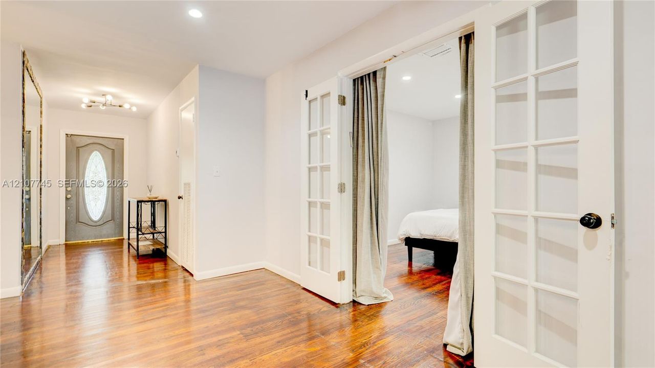 Entryway featuring wood-finish flooring, recessed lighting, and a front door with an oval glass insert, complemented by white French doors and a floor-to-ceiling wall mirror