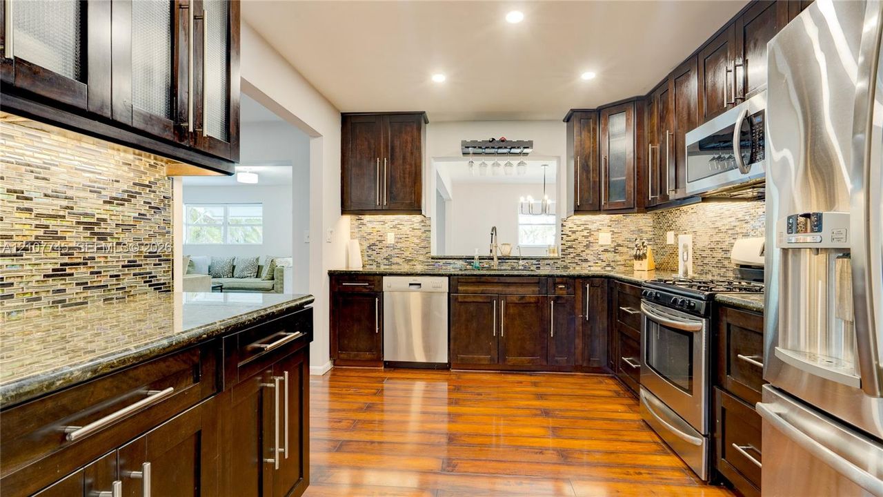 Kitchen featuring dark wood cabinetry, stainless steel appliances, multi-tonal tile backsplash, stone-surface countertops, and wood-finish flooring