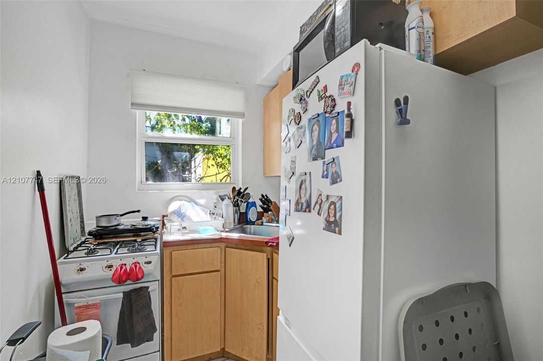 Kitchen featuring light-finish wood cabinetry, a stainless steel sink, a gas range, and a window with a roller shade