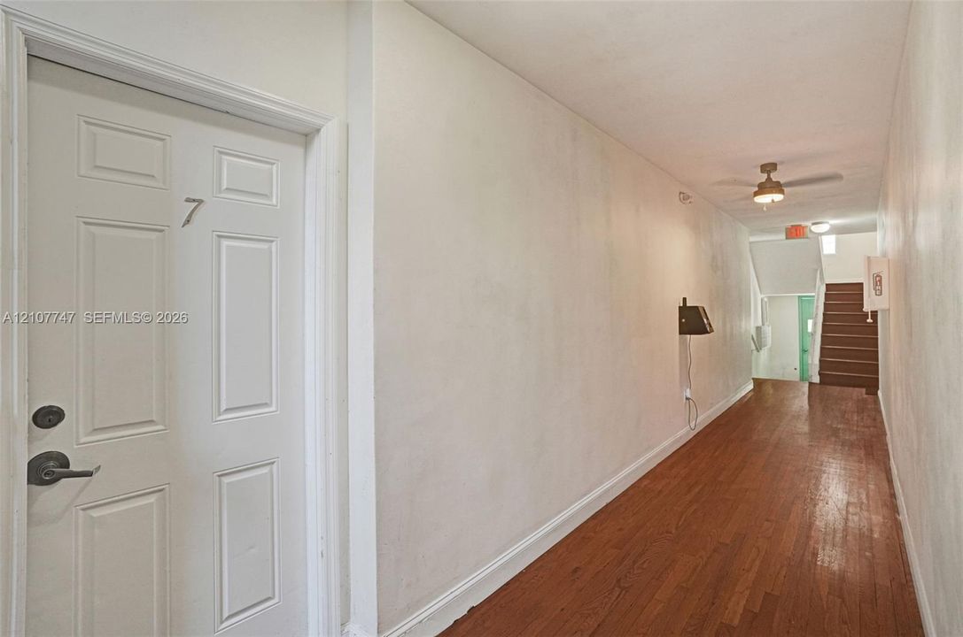 Hallway featuring wood-finish flooring, white walls, a flush-mount ceiling light fixture, and a ceiling fan