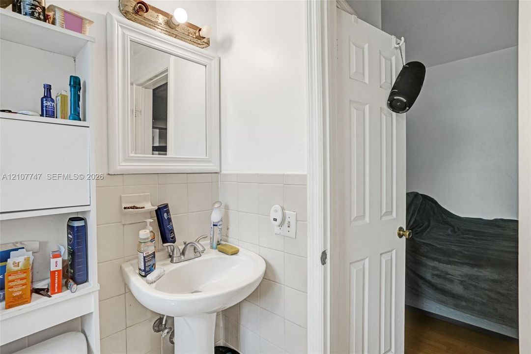 Pedestal sink featuring a chrome dual-handle faucet, framed wall mirror, built-in shelving unit, and tiled wall surfacing