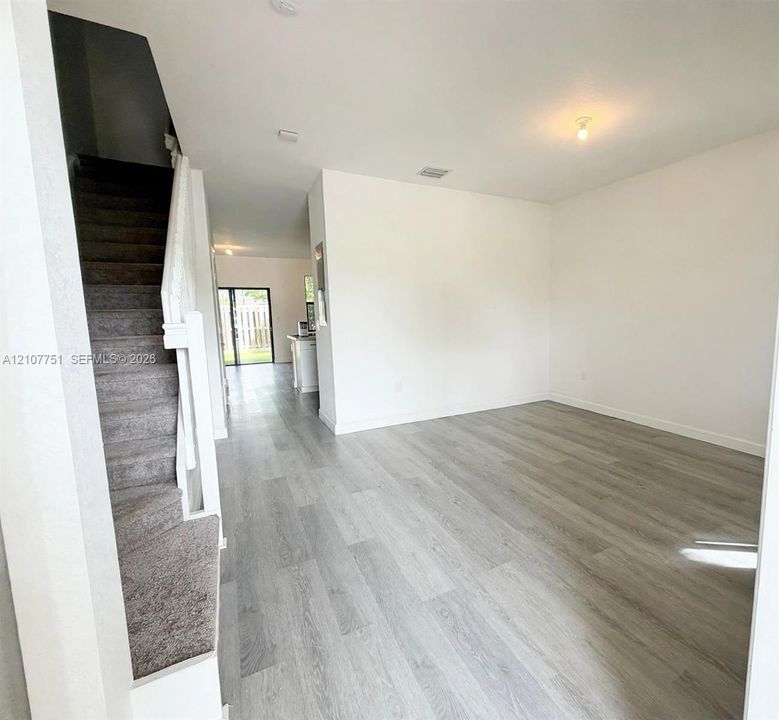 Open-concept interior featuring light-toned wood-finish flooring, a carpeted staircase with a white railing, and sliding glass doors