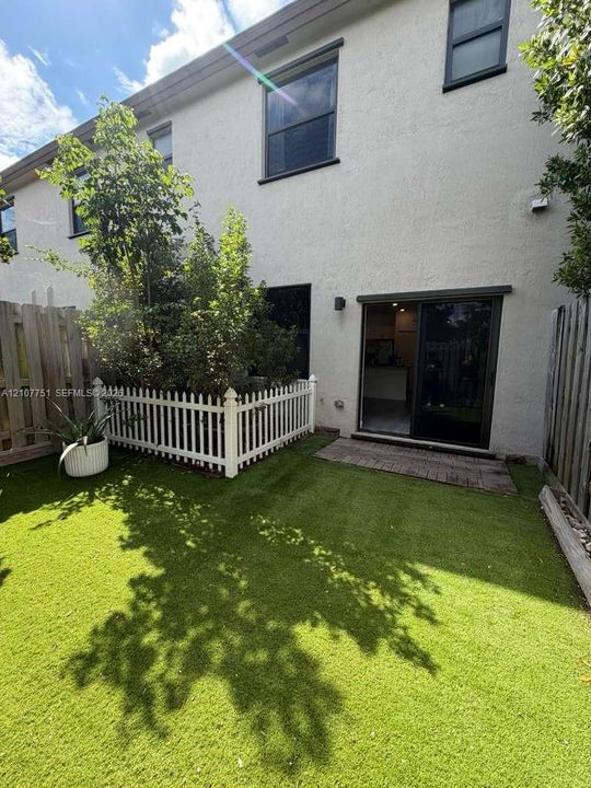 Enclosed backyard featuring synthetic turf, wood-tone privacy fencing, a white picket-style enclosure, and a paved patio area