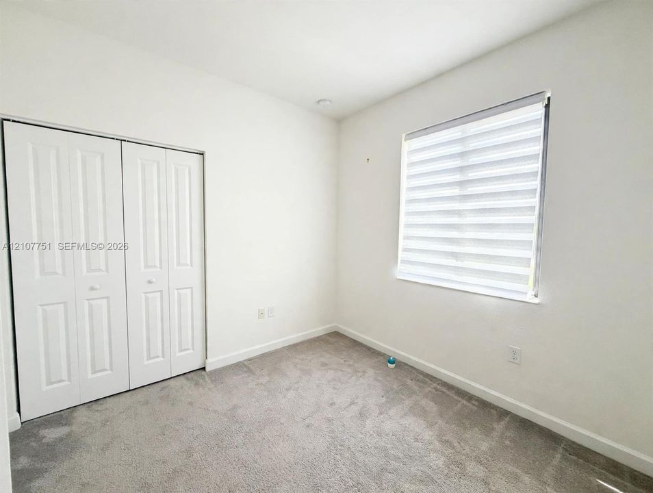 Neutral-toned carpeting, white walls, dual-paneled closet doors, and a window fitted with horizontal layered shades