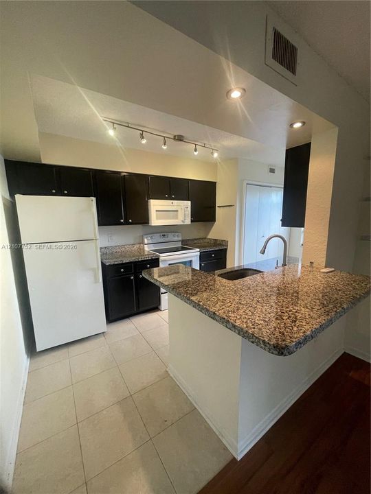 Kitchen featuring dark cabinetry, stone-surface countertops, tile flooring, a peninsula breakfast bar, and stainless steel undermount sink