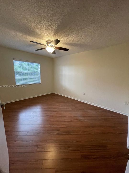 Interior space featuring wood-finish flooring, a ceiling fan with integrated light fixture, and a window with horizontal blinds