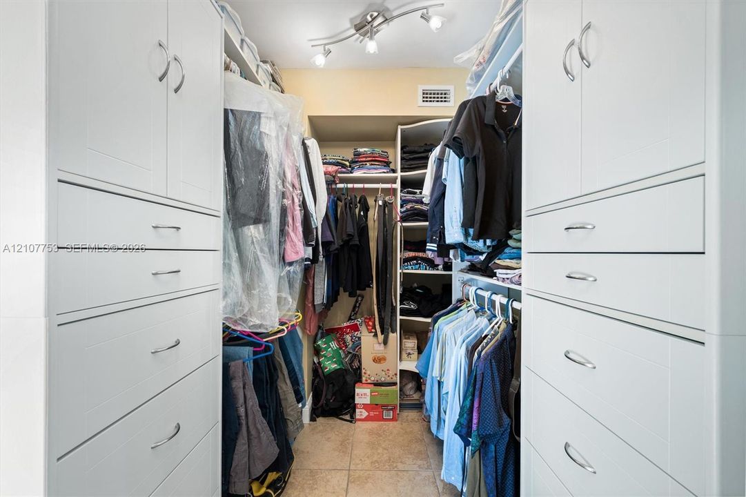 Walk-in closet featuring extensive built-in white cabinetry, multi-tiered shelving, drawer storage, chrome hardware, and overhead track lighting