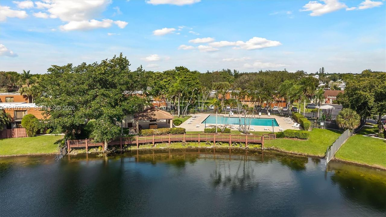 Waterfront area featuring a swimming pool, covered pavilion, wooden boardwalk, and mature landscaping