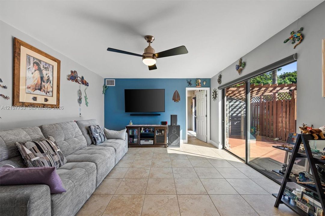 Living area featuring tile flooring, a ceiling fan with integrated lighting, a vibrant blue accent wall, and expansive sliding glass doors