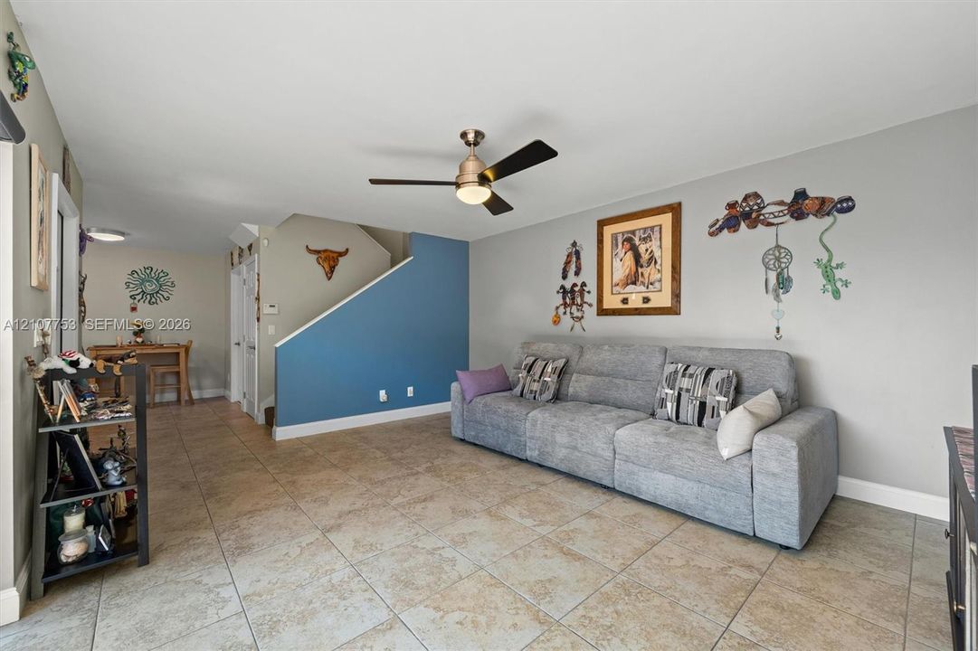 Living area featuring ceramic tile flooring, a multi-tone painted wall finish, and a ceiling fan with integrated lighting