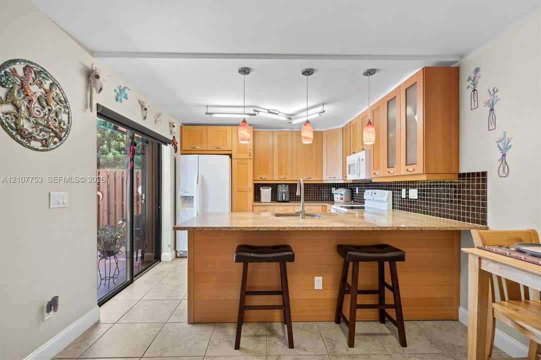 Kitchen featuring wood cabinetry, solid surface countertops, a mosaic tile backsplash, tile flooring, and glass-paneled pendant lighting