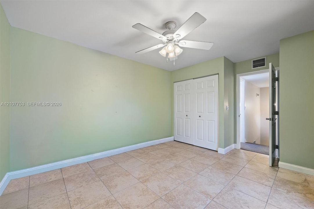 Room featuring tile flooring, a multi-blade ceiling fan with integrated light fixture, and a white double-door closet