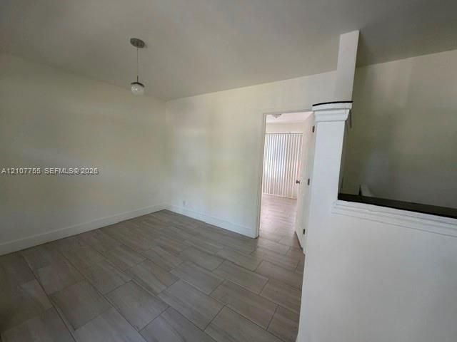 Interior space featuring wood-finish flooring, a neutral color palette, a single-bulb pendant light fixture, and a half-wall with a cap molding detail