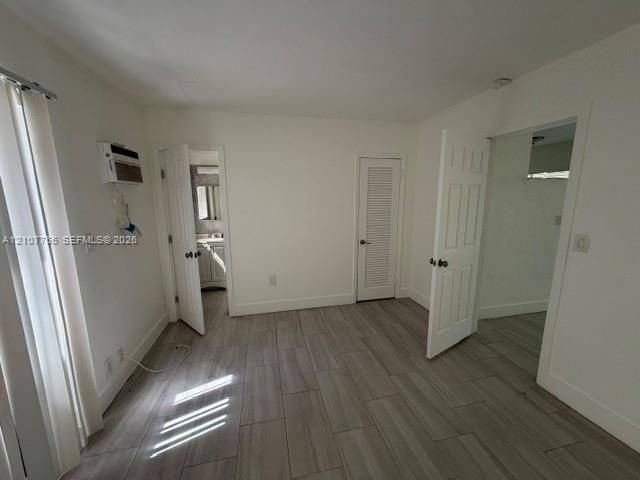 Interior space featuring wood-finish tile flooring, white six-panel interior doors, a louvered closet door, and a wall-mounted climate control unit