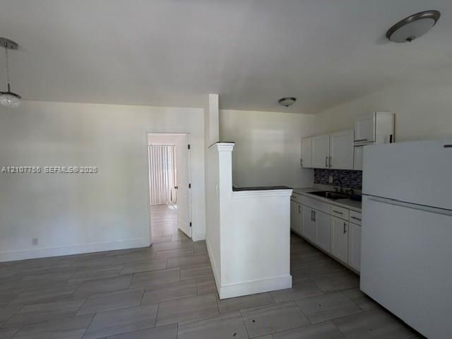 Kitchen featuring white shaker-style cabinetry, a decorative mosaic tile backsplash, solid-surface countertops, and wood-finish tile flooring throughout