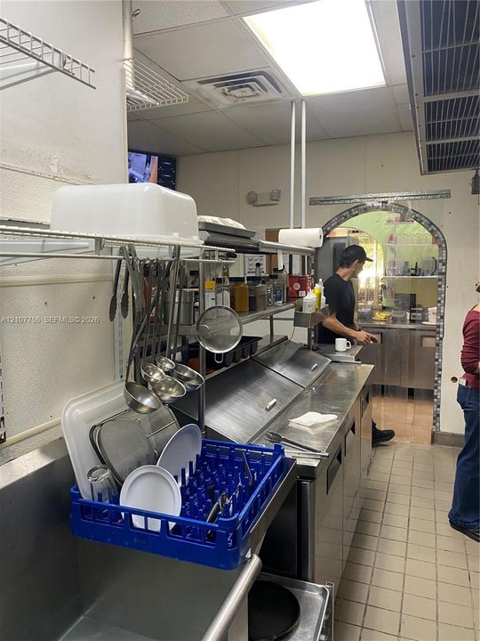 Commercial kitchen featuring stainless steel food preparation stations, built-in ventilation hood system, drop ceiling with integrated lighting, and ceramic tile flooring