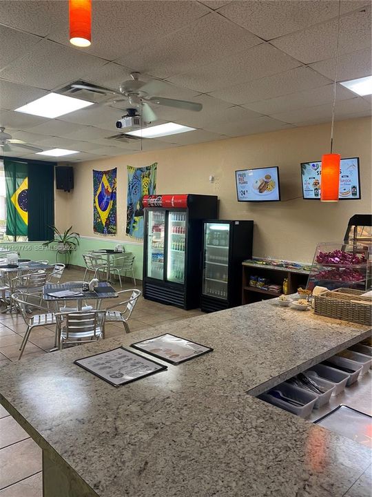 Commercial space featuring a stone-topped service counter, drop ceiling with recessed lighting, suspended pendant fixtures, and tile flooring