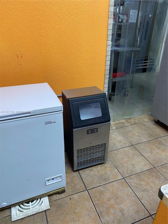 Stainless steel commercial ice machine and white chest freezer situated on neutral-toned square ceramic tile flooring