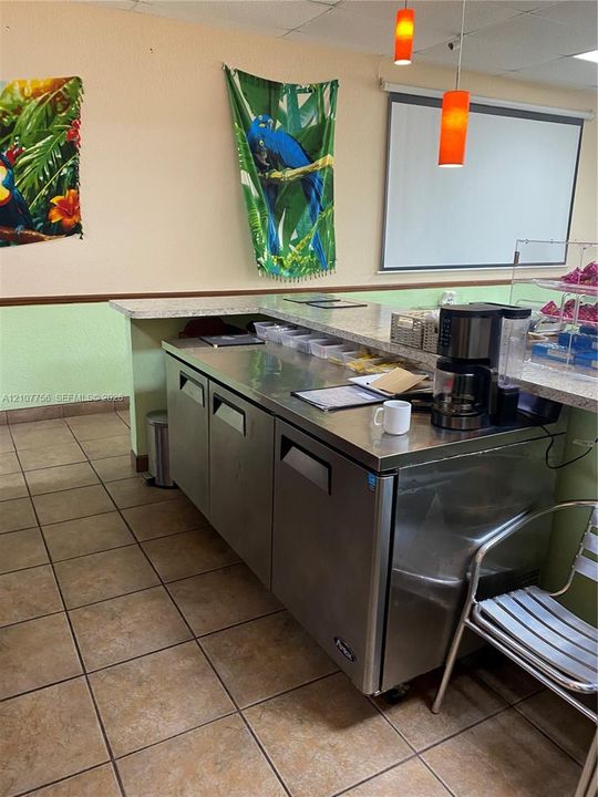 Service counter featuring a speckled stone-finish countertop, stainless steel under-counter cabinetry, ceramic tile flooring, and dual pendant lighting fixtures