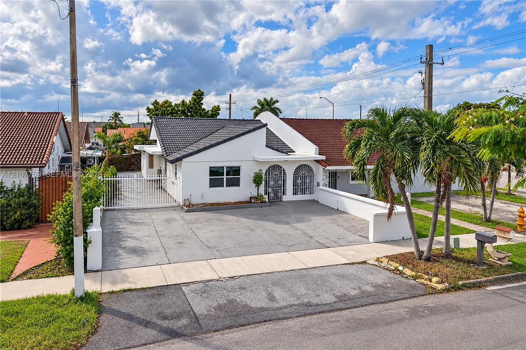 White exterior facade featuring a multi-gabled tile roof, concrete driveway, and arched entryway with security screening