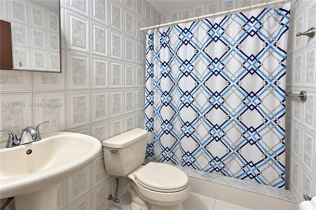 Full-height tiled walls, pedestal sink with polished chrome dual-handle faucet, integrated tub and shower combination, and wall-mounted medicine cabinet