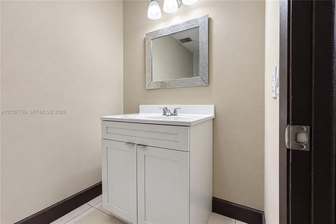 White vanity with shaker-style cabinetry, integrated basin, chrome faucet, rectangular framed mirror, and three-bulb vanity light fixture