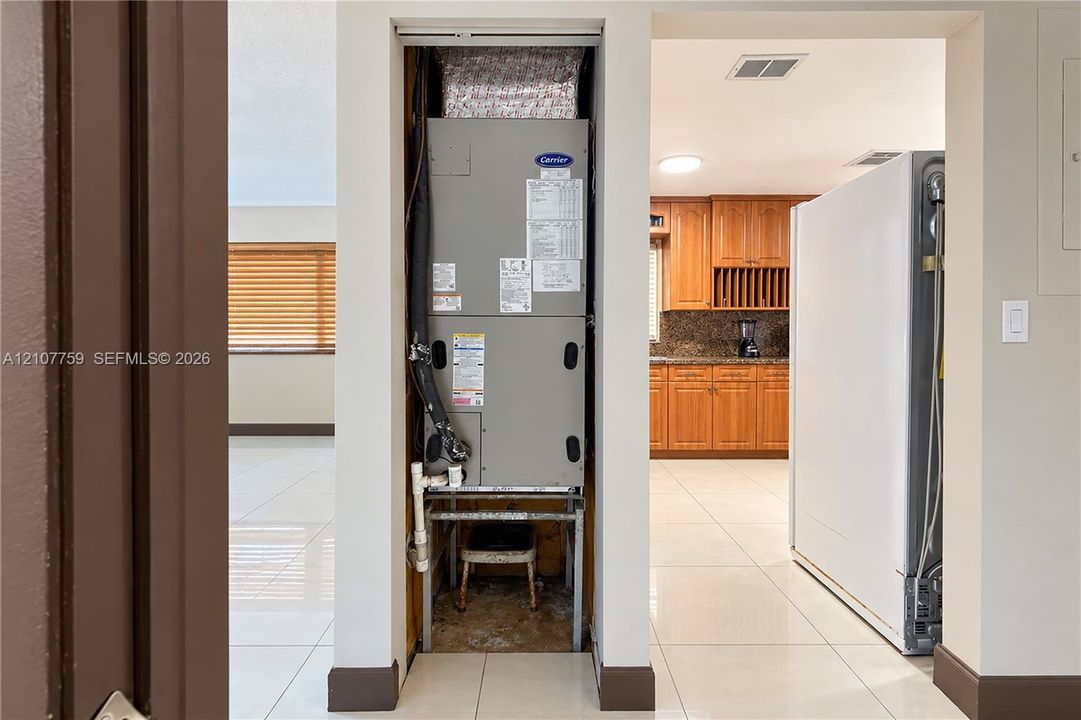 Dedicated utility closet featuring a Carrier HVAC unit, positioned alongside a kitchen equipped with wood-finish cabinetry, stone-surfaced countertops, and tiled flooring