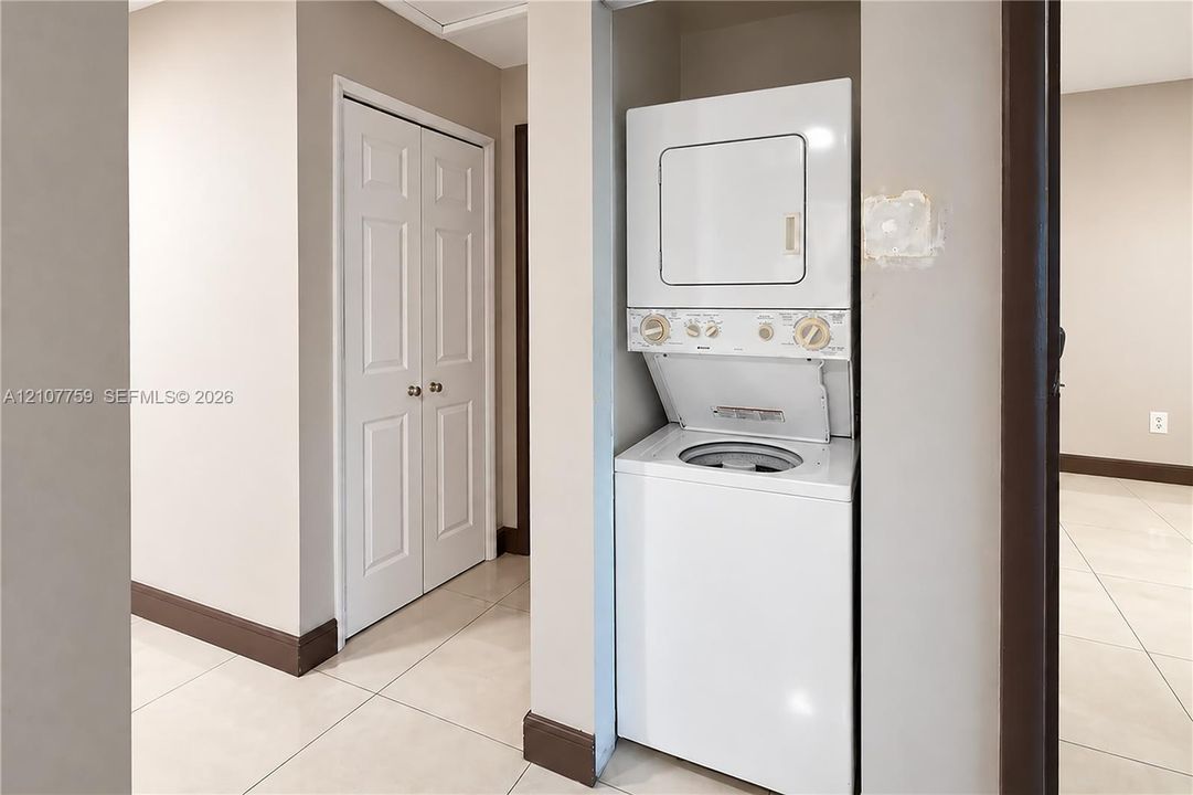 Stacked white laundry unit housed in a recessed alcove, paired with a white bifold door closet and light-toned tile flooring