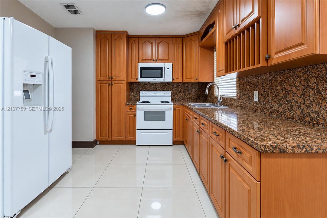 Kitchen featuring honey-toned wood cabinetry, stone-finish countertops, tile flooring, built-in microwave, and white appliances