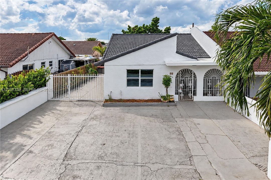White exterior facade featuring a concrete driveway, gated side entrance, tiled roof, and decorative arched security grilles