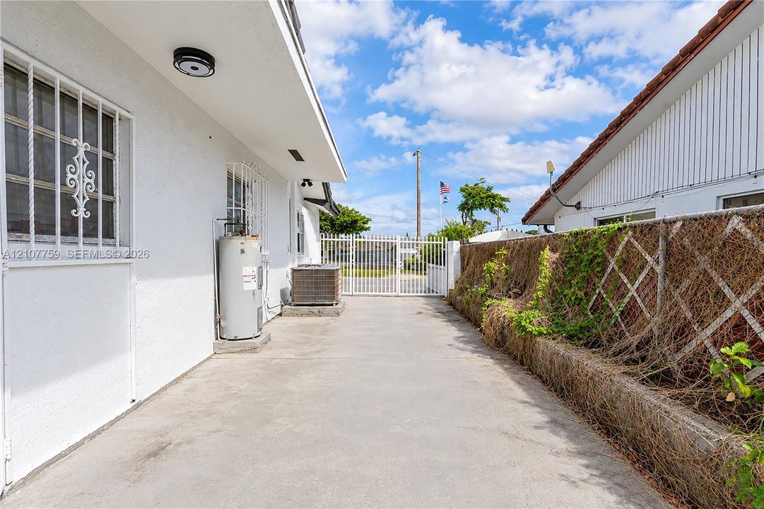 Side exterior area featuring a concrete driveway, white metal security gate, white stucco wall finish, and white metal window security bars